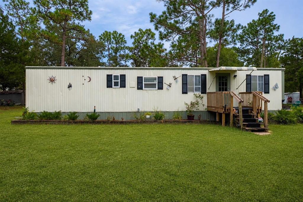 A single-story mobile home with a wooden porch sits on a grassy lot with trees — 5108 W FIELD STREET, HOMOSASSA, FL
