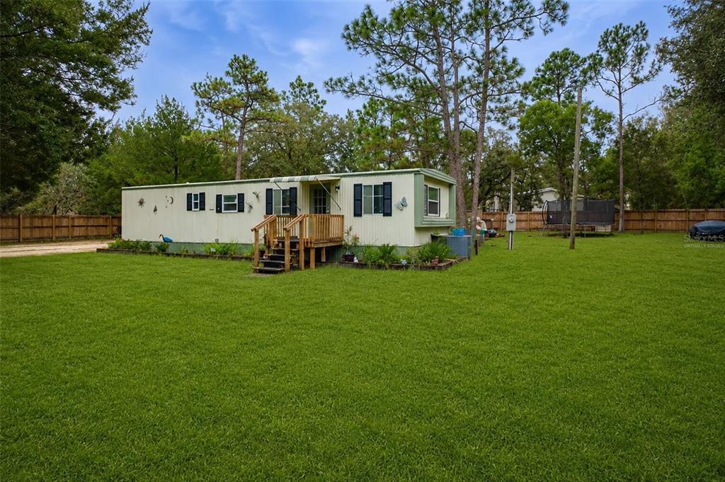 A single-story mobile home sits on a large grassy lot surrounded by pine trees — 5108 W FIELD STREET, HOMOSASSA, FL