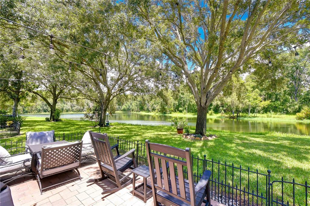 A patio with outdoor furniture overlooks a grassy lawn, large trees, and a pond — 5301 BRADBURY COURT, TAMPA, FL