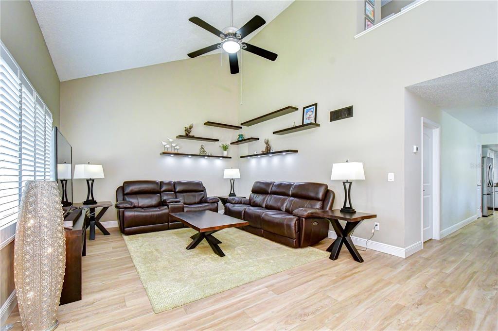 A living room features brown leather sofas, a coffee table, and floating shelves on the wall — 5301 BRADBURY COURT, TAMPA, FL