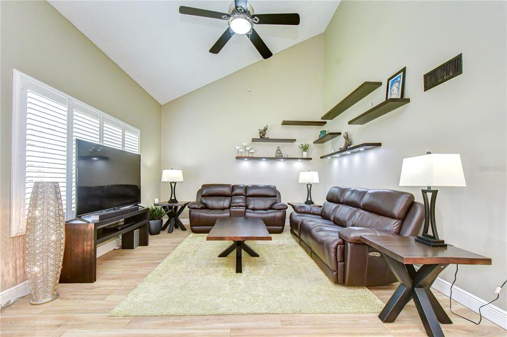 A living room features brown leather furniture, a large television, and tiered wall-mounted shelves — 5301 BRADBURY COURT, TAMPA, FL