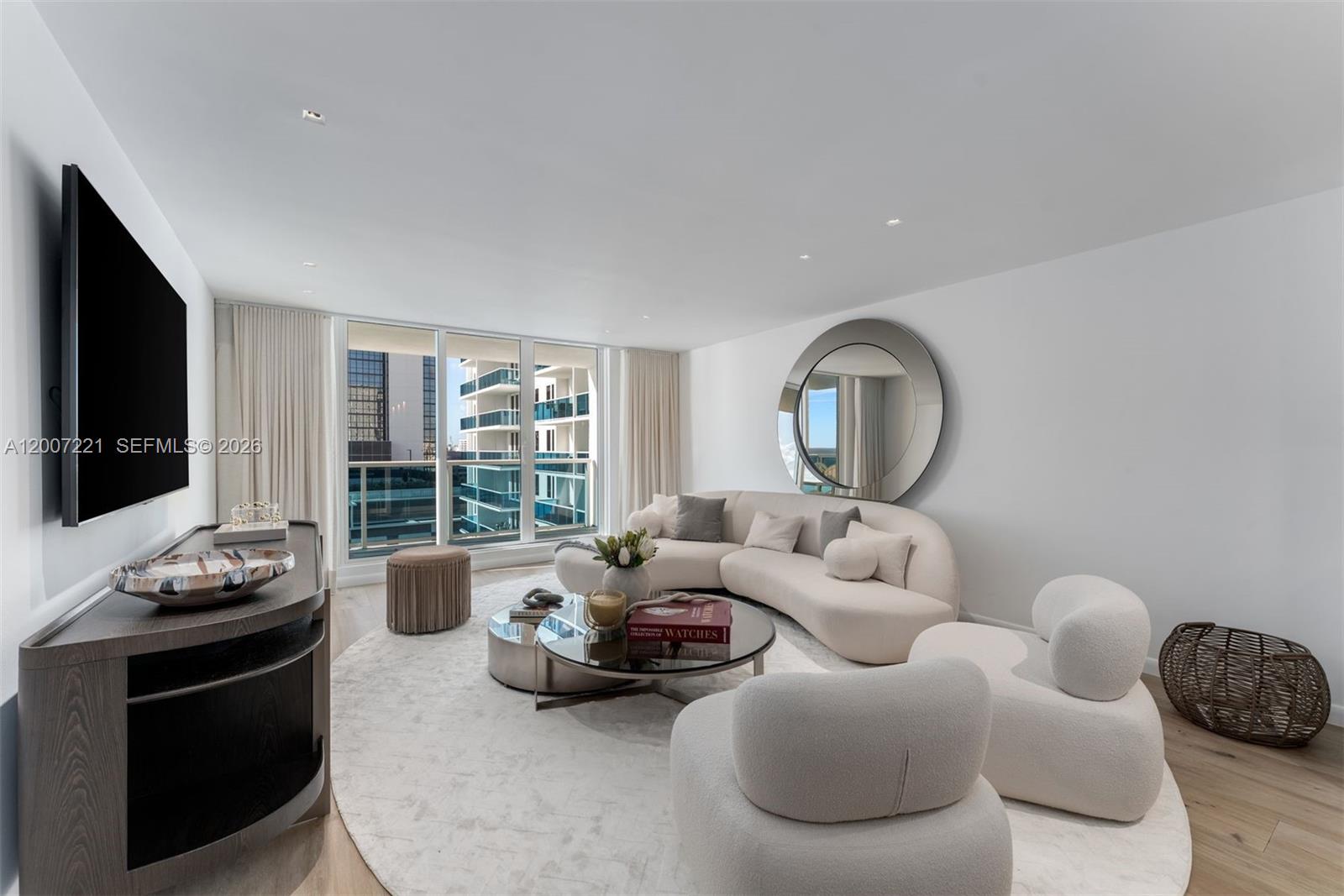 A modern living room features a curved sofa, two armchairs, and a large circular mirror — 2301 Collins Ave # 902, Miami Beach FL 33139, MIAMI BEACH, FL