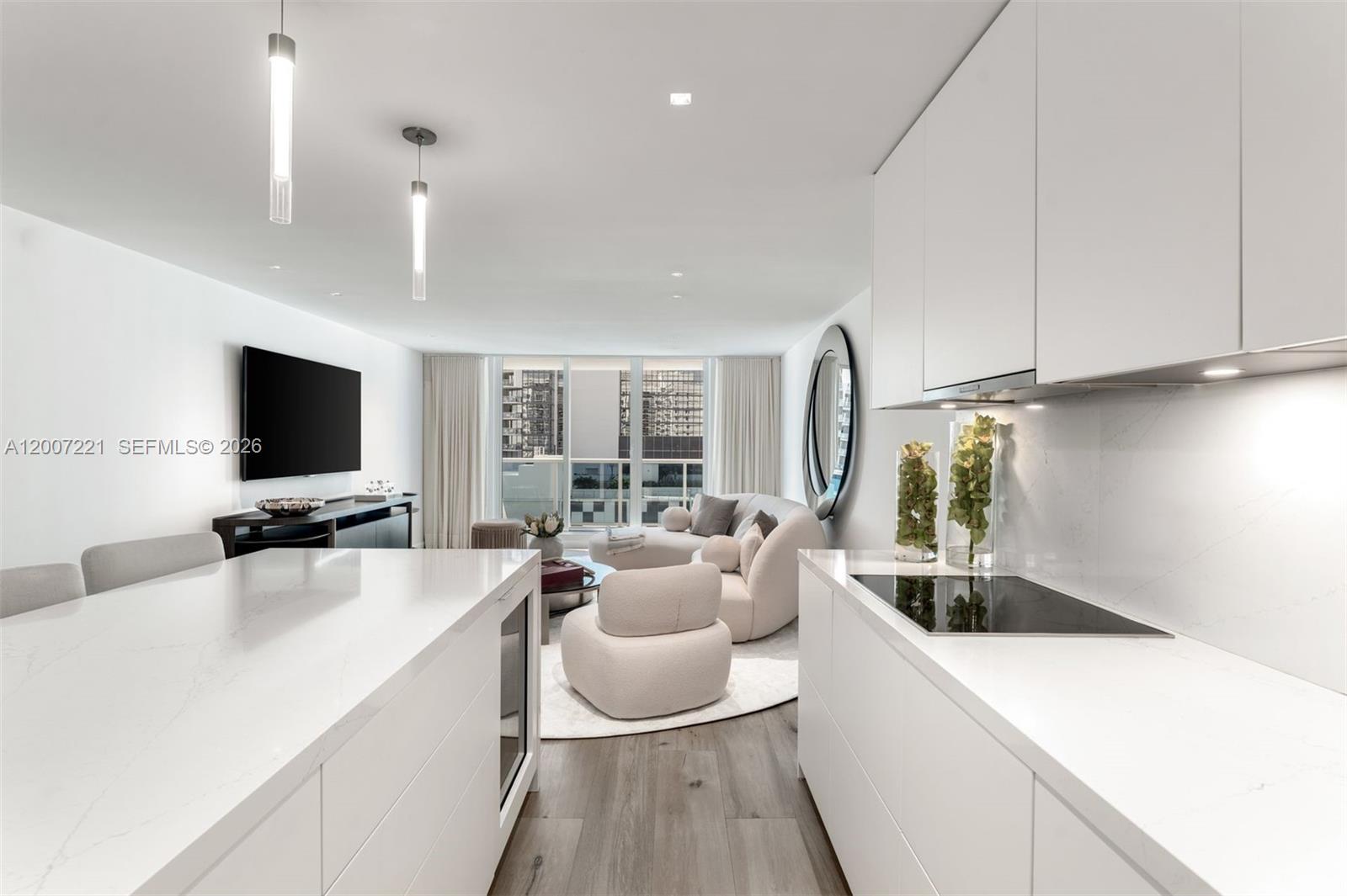 A modern white kitchen with an island overlooks a living area with floor-to-ceiling windows — 2301 Collins Ave # 902, Miami Beach FL 33139, MIAMI BEACH, FL