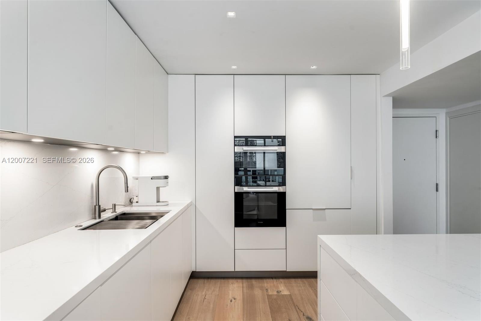 A modern kitchen features white flat-panel cabinetry, integrated appliances, and light wood flooring — 2301 Collins Ave # 902, Miami Beach FL 33139, MIAMI BEACH, FL