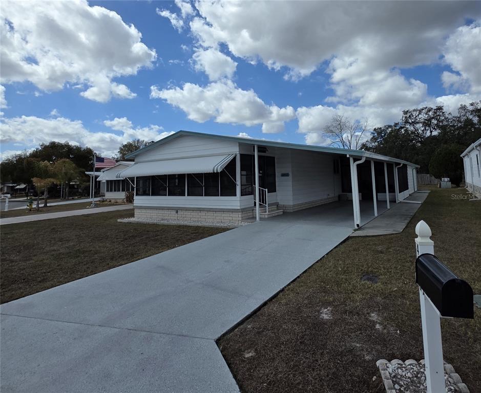 A white manufactured home features a screened-in front porch and a long concrete driveway — 4843 BLANCO DRIVE, ZEPHYRHILLS, FL