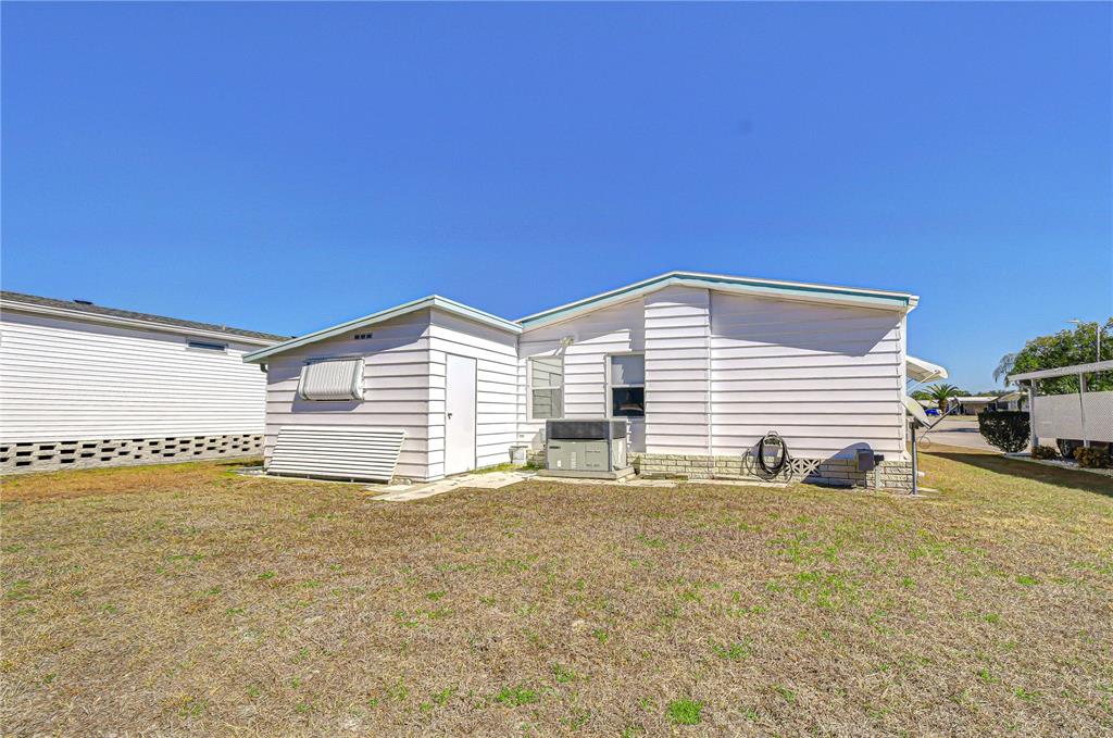 The exterior of a light-colored mobile home features a small yard and HVAC unit — 4843 BLANCO DRIVE, ZEPHYRHILLS, FL