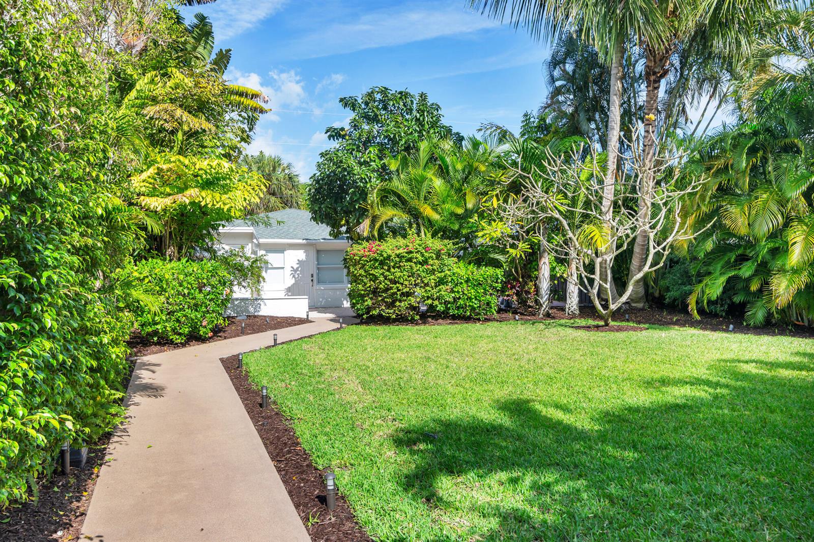 A concrete walkway leads through a lush, green yard toward a small white house — 439 28th Street, West Palm Beach FL 33407, WEST PALM BEACH, FL