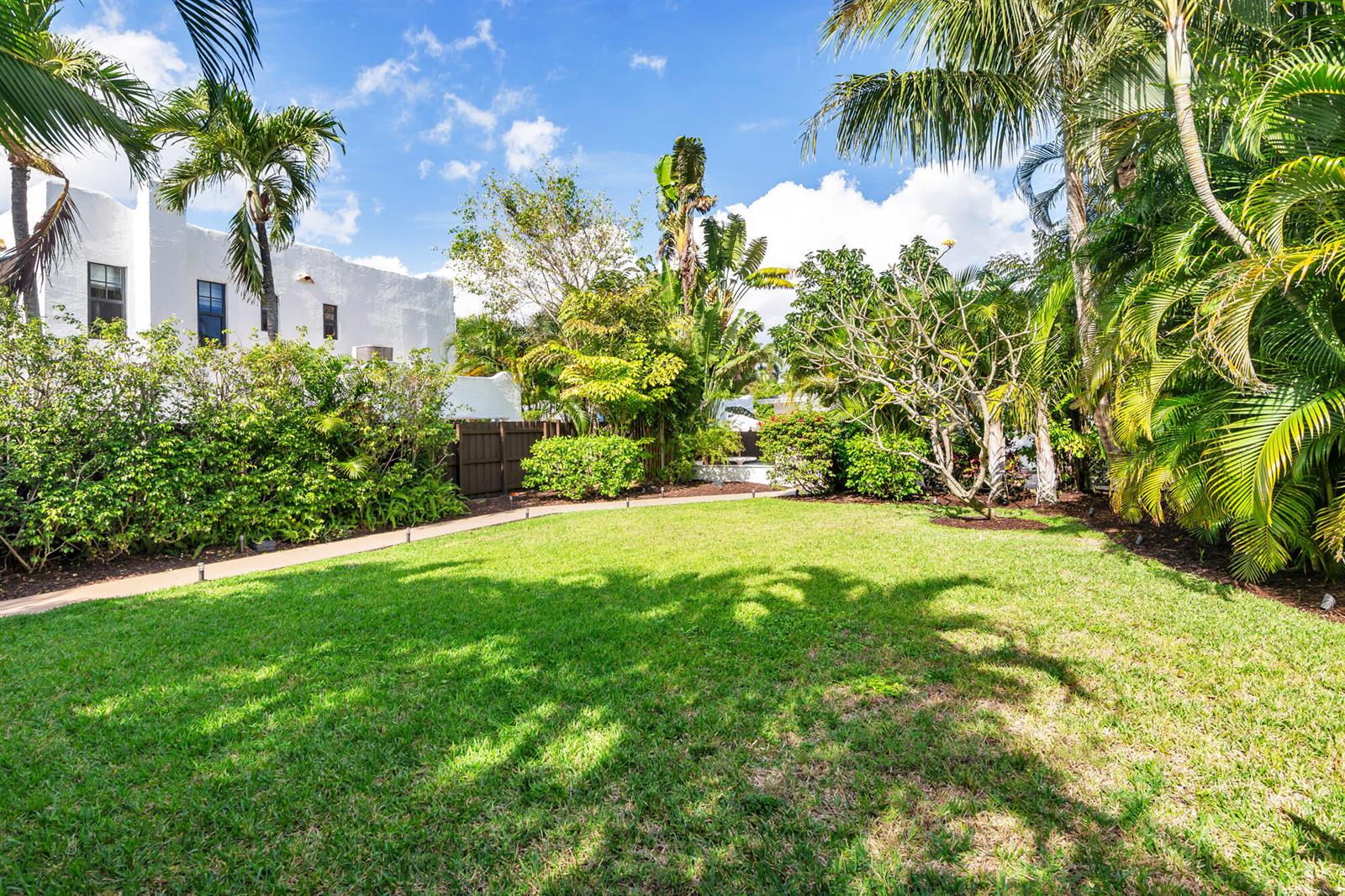 A grassy backyard features a paved walkway, lush tropical landscaping, and a white building exterior — 439 28th Street, West Palm Beach FL 33407, WEST PALM BEACH, FL