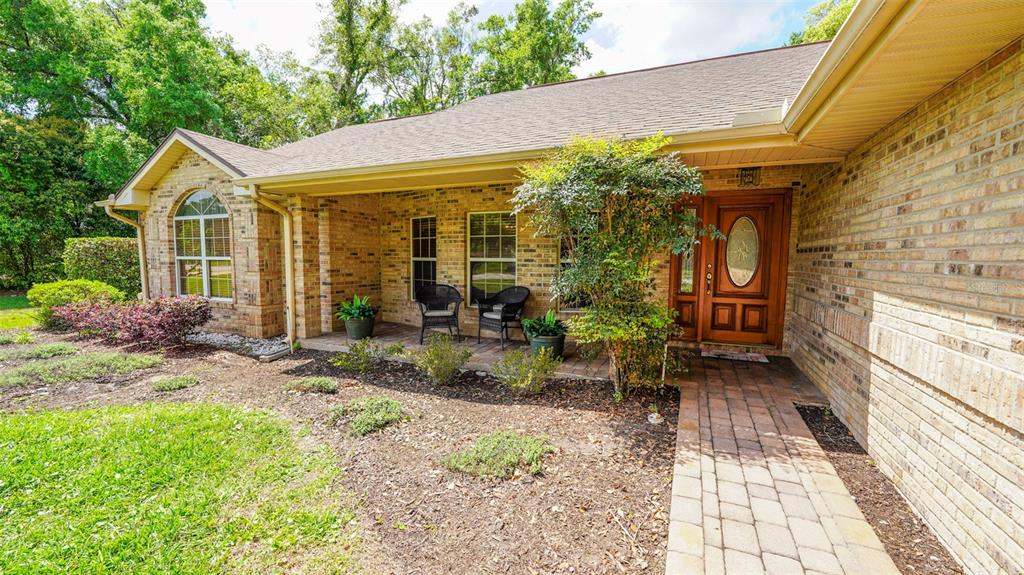 A brick house exterior features a covered front porch, a wooden door, and a walkway — 204 BRYNWOOD LANE, SANFORD, FL