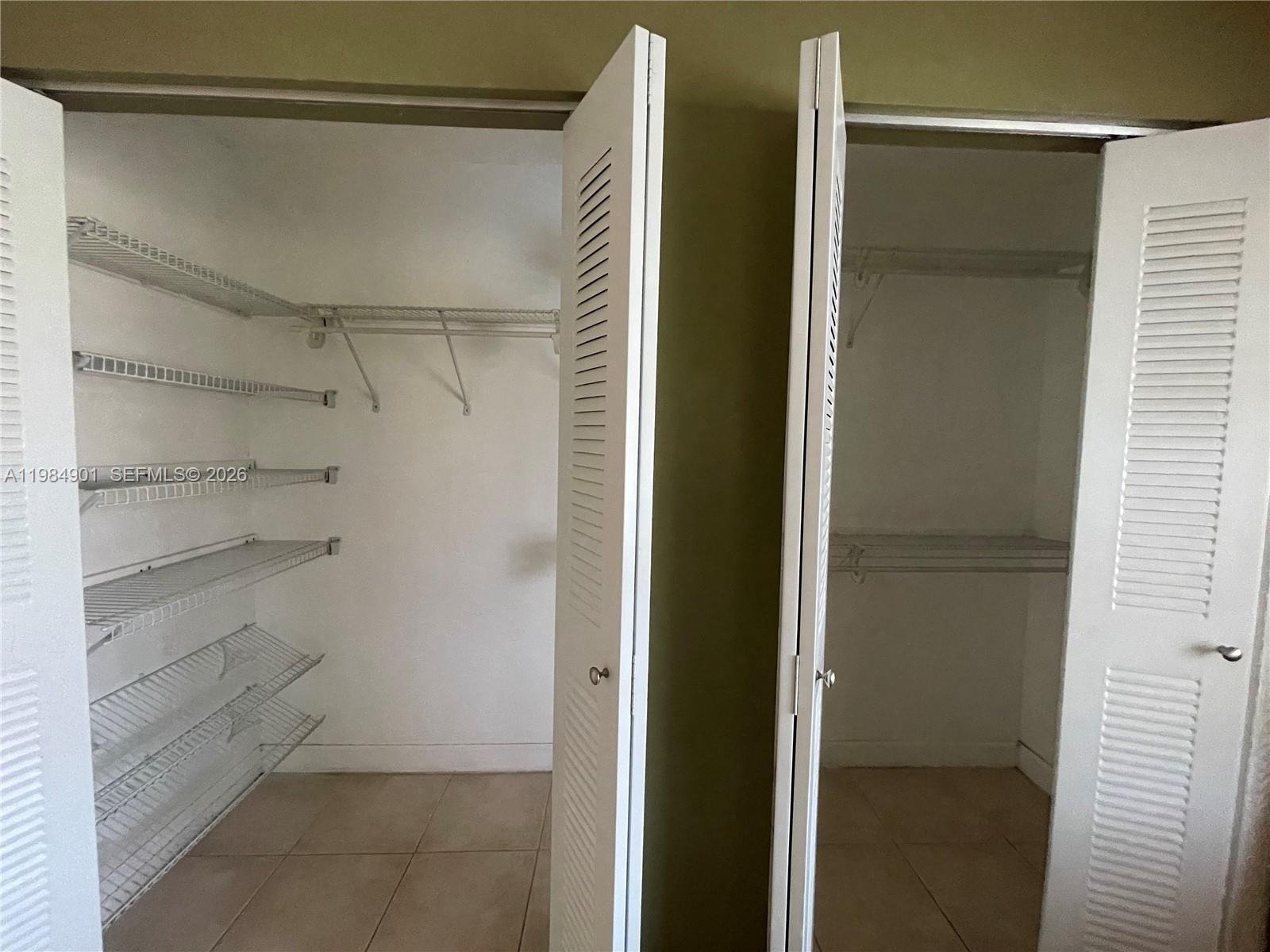 Two side-by-side closets feature white louvered doors, wire shelving, and light-colored tile flooring — 8600 SW 109th Ave # 220, Miami FL 33173, MIAMI, FL