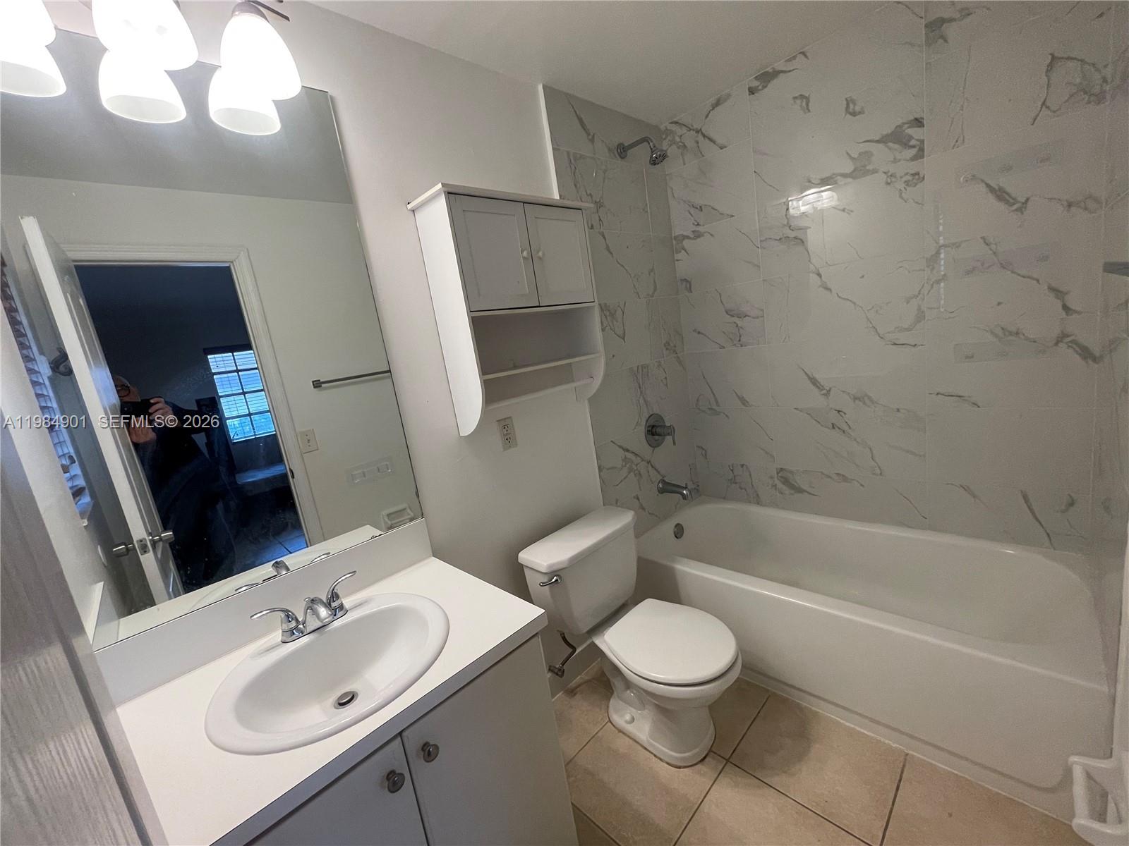 A bathroom features a white vanity, a toilet, and a bathtub with marble-patterned tile walls — 8600 SW 109th Ave # 220, Miami FL 33173, MIAMI, FL
