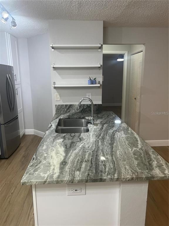 A kitchen island with a granite countertop and stainless steel sink sits before open shelving — 956 SALT POND PLACE UNIT 204, ALTAMONTE SPRINGS, FL