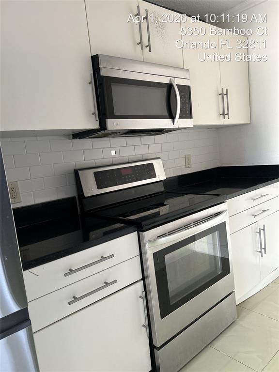 A kitchen features white cabinets, stainless steel appliances, and a black countertop with subway tile — 5344 BAMBOO COURT, ORLANDO, FL