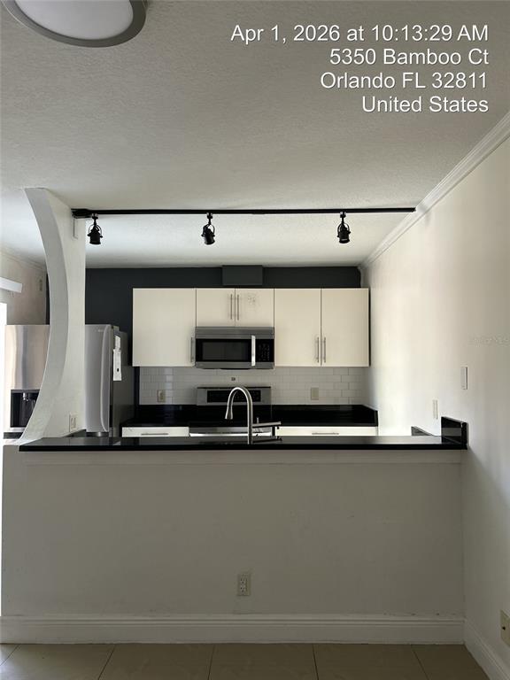 A kitchen features white cabinets, black countertops, stainless steel appliances, and track lighting — 5344 BAMBOO COURT, ORLANDO, FL
