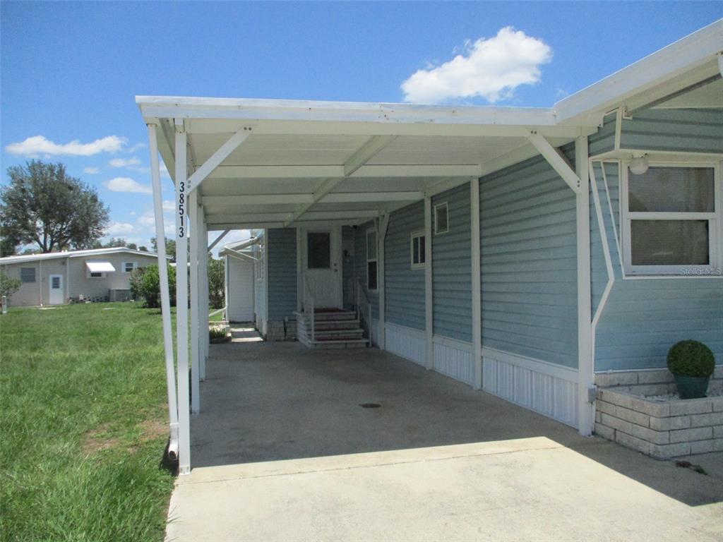 A light blue mobile home features a concrete carport and a small front porch — 38513 WILLOUGHBY DRIVE, ZEPHYRHILLS, FL