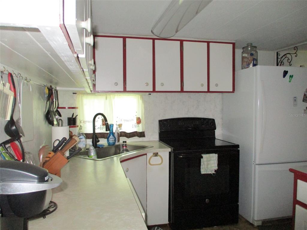A kitchen features white cabinets with red trim, a black stove, and a corner sink — 38513 WILLOUGHBY DRIVE, ZEPHYRHILLS, FL