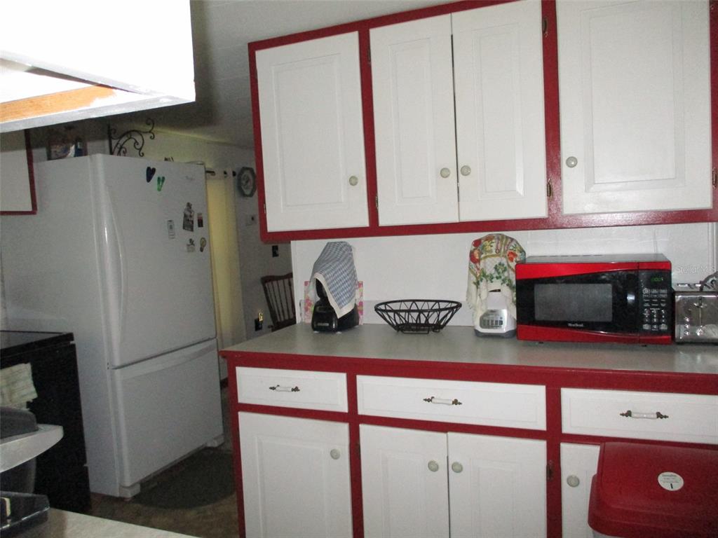 A kitchen features white cabinets with red trim, a red microwave, and a white refrigerator — 38513 WILLOUGHBY DRIVE, ZEPHYRHILLS, FL