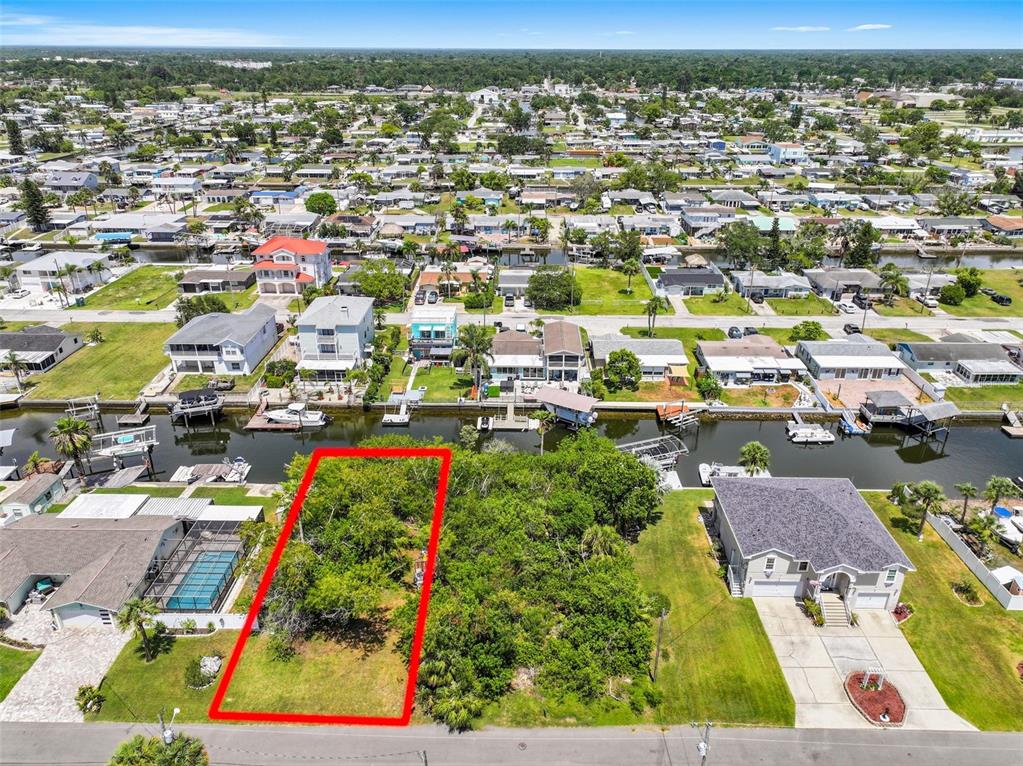 An aerial view shows a vacant, tree-covered residential lot outlined in red along a canal — 13330 SUNFISH DRIVE, HUDSON, FL