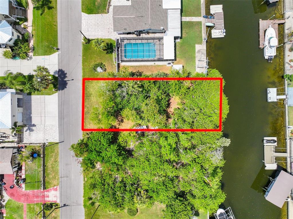 An aerial view shows a rectangular, tree-covered vacant lot situated between a road and canal — 13330 SUNFISH DRIVE, HUDSON, FL