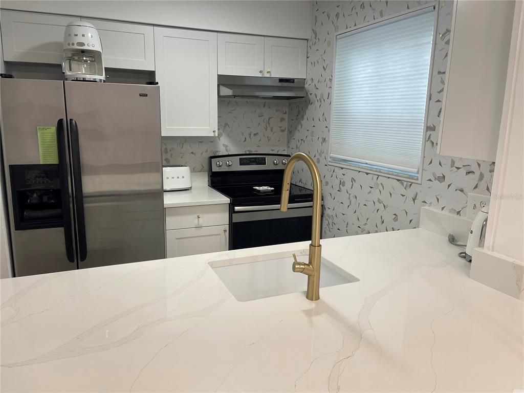 A modern kitchen features white cabinets, stainless steel appliances, a gold faucet, and quartz countertops — 6826 STONES THROW CIRCLE N UNIT 11108, ST PETERSBURG, FL