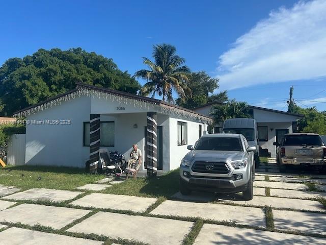 A white single-story house with a paved driveway and a person sitting on the porch — 3066 NW 92nd St, Miami FL 33147, MIAMI, FL