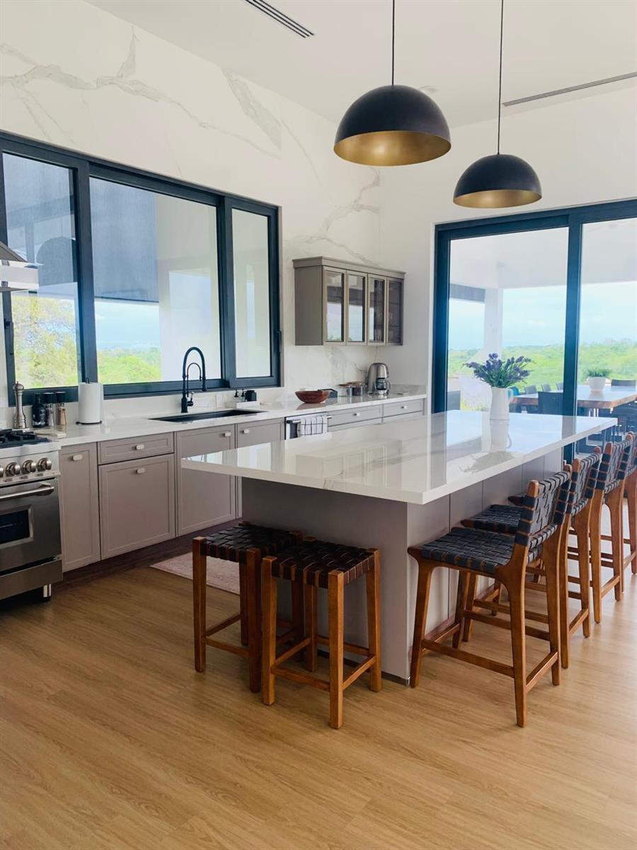 A modern kitchen features a large island, gray cabinetry, marble-look walls, and expansive outdoor views — Las Lagartijas San Carlos, Cocle, FL