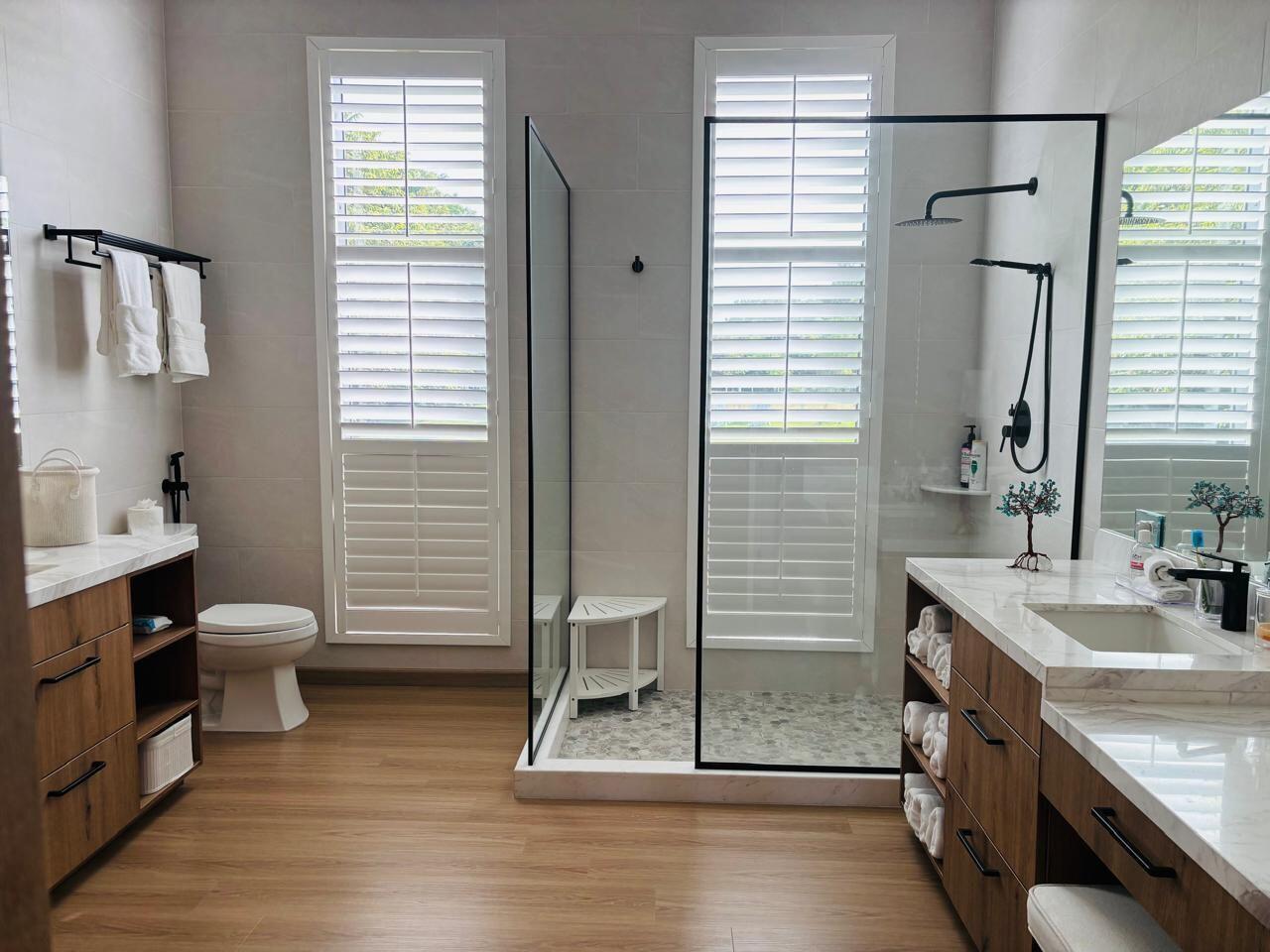 A modern bathroom features wood vanities, a glass-enclosed shower, and white plantation shutters — Las Lagartijas San Carlos, Cocle, FL