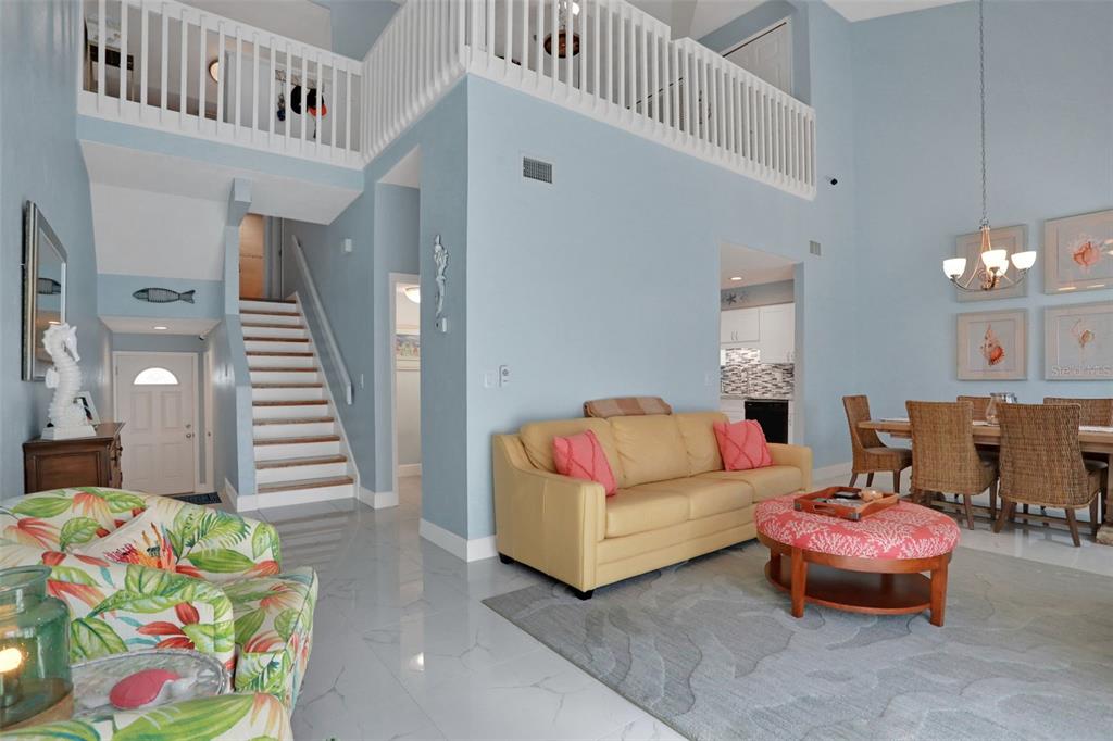A living room with light blue walls, a yellow sofa, and a staircase to a loft — 33 SEA HAVEN DRIVE, PONCE INLET, FL