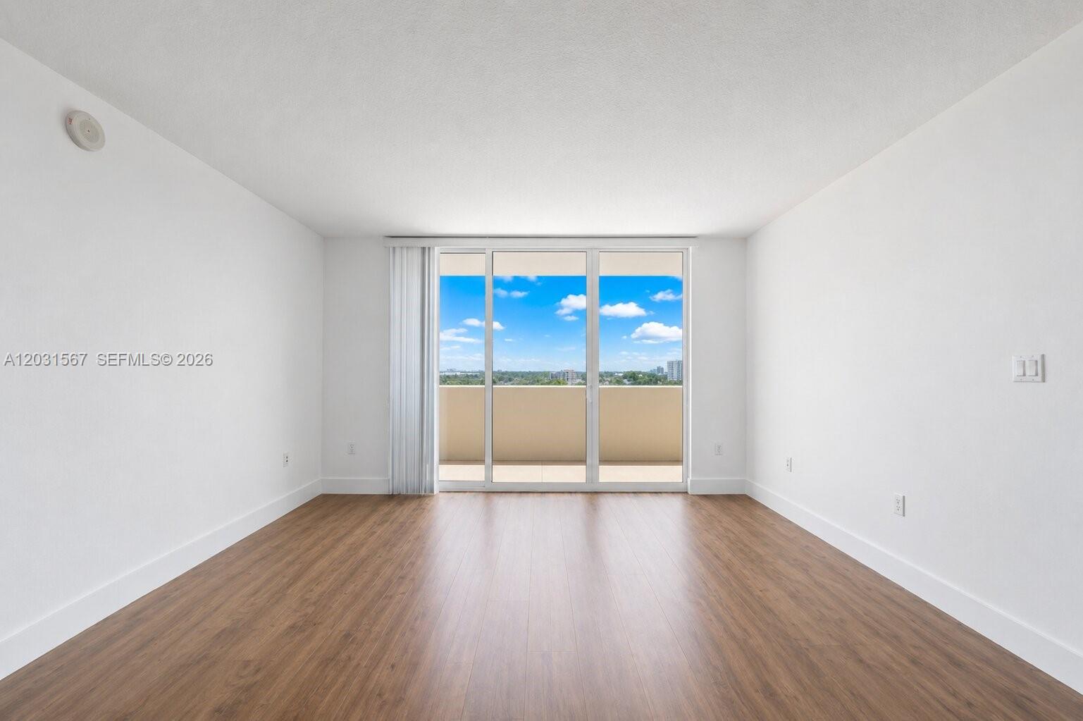 An empty room with wood-look flooring, white walls, and a sliding glass door to a balcony — 3232 SW 22nd Ter # 802, Miami FL 33145, MIAMI, FL