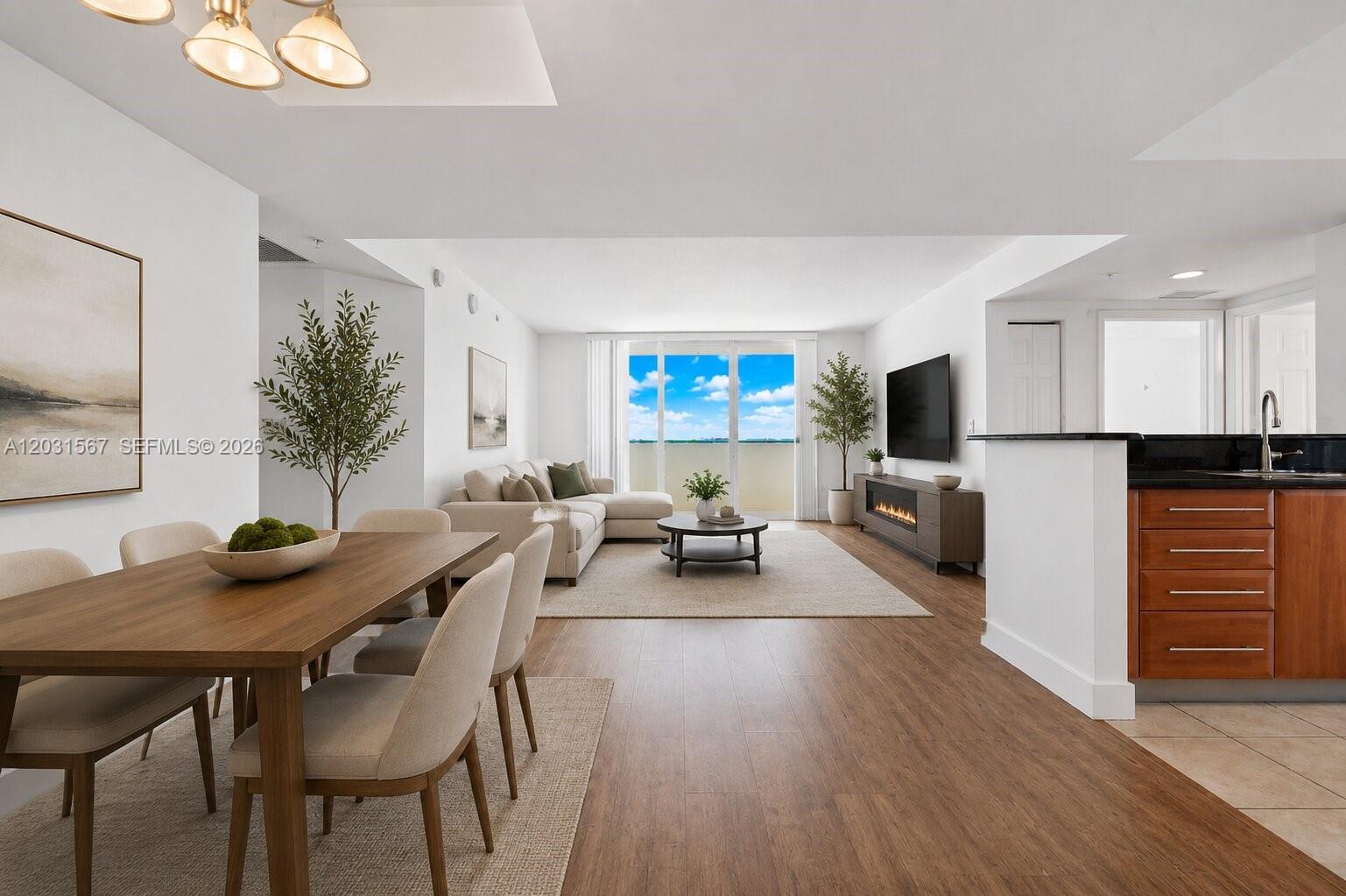 An open-concept living and dining area features wood flooring, a neutral sofa, and balcony views — 3232 SW 22nd Ter # 802, Miami FL 33145, MIAMI, FL
