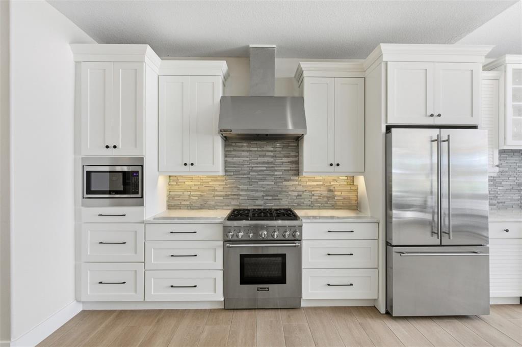 A modern kitchen features white cabinetry, stainless steel appliances, and a horizontal tile backsplash — 4733 CHULUOTA ROAD, ORLANDO, FL