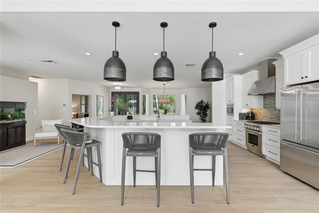 A modern kitchen features a white island with three gray stools and three pendant lights — 4733 CHULUOTA ROAD, ORLANDO, FL