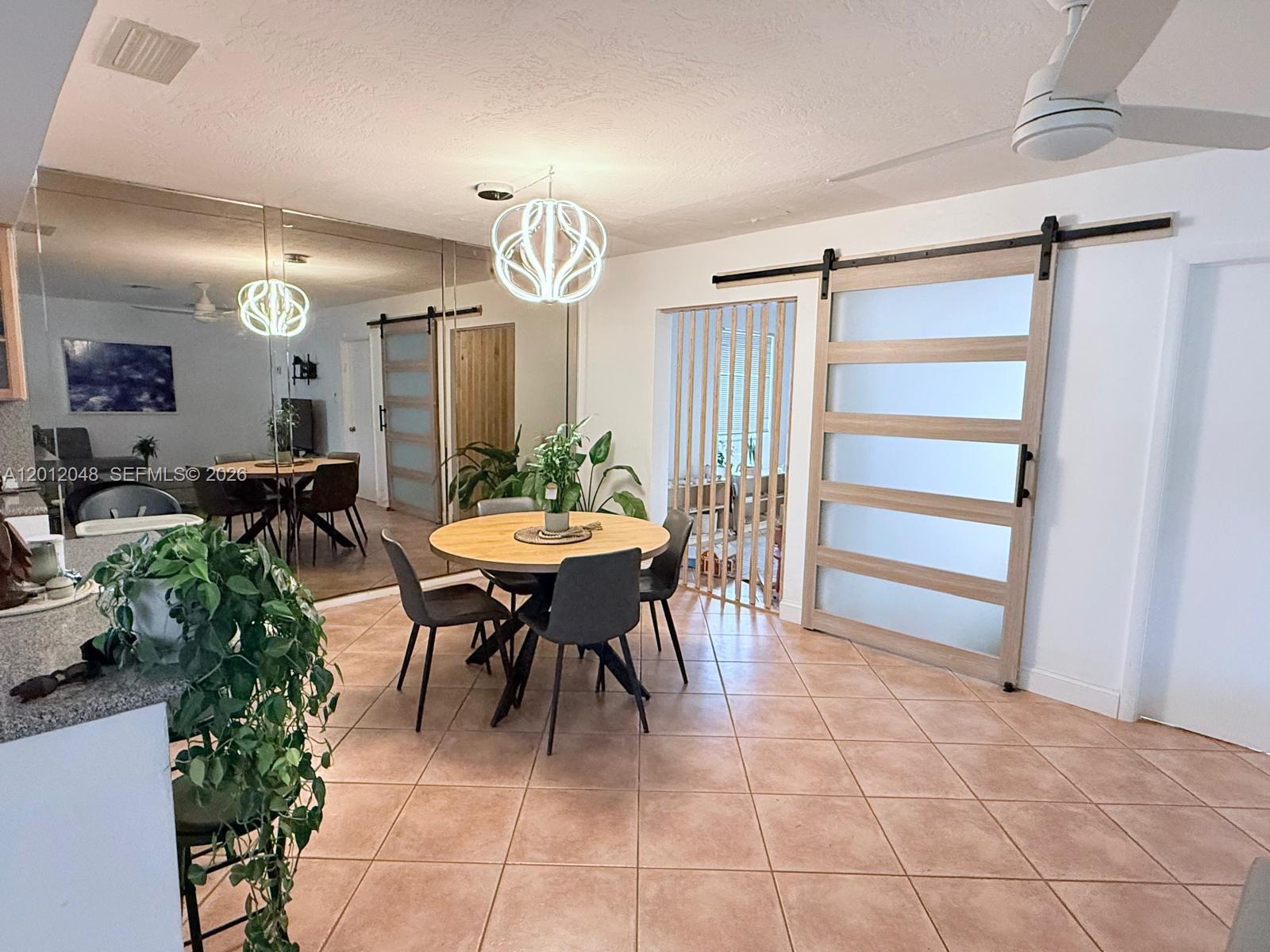 A dining area features a round table, modern chairs, a barn door, and mirrored walls — 9356 Byron Ave, Surfside FL 33154, SURFSIDE, FL