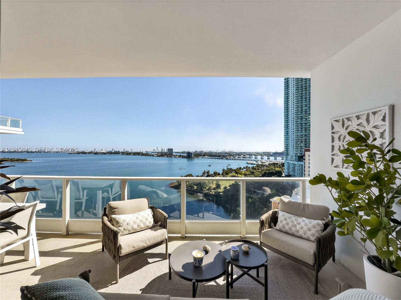 A balcony with two armchairs, two round tables, and a panoramic view of the bay — 2020 N Bayshore Dr # 1603, Miami FL 33137, MIAMI, FL