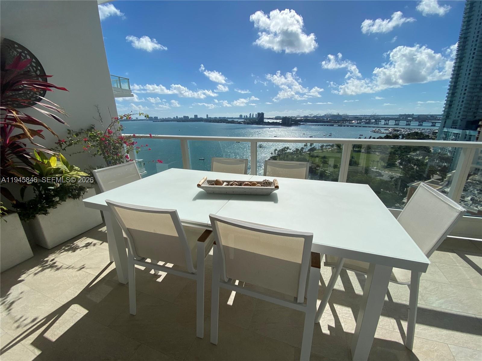 A white dining set sits on a balcony overlooking the ocean and city skyline — 2020 N Bayshore Dr # 1603, Miami FL 33137, MIAMI, FL