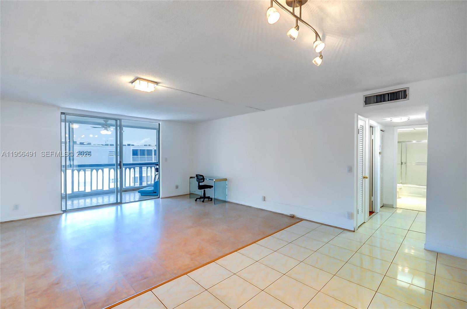 A living area with tile flooring, a glass desk, and a sliding door to a balcony — 301 NE 14th Ave # 702, Hallandale Beach FL 33009, HALLANDALE BEACH, FL