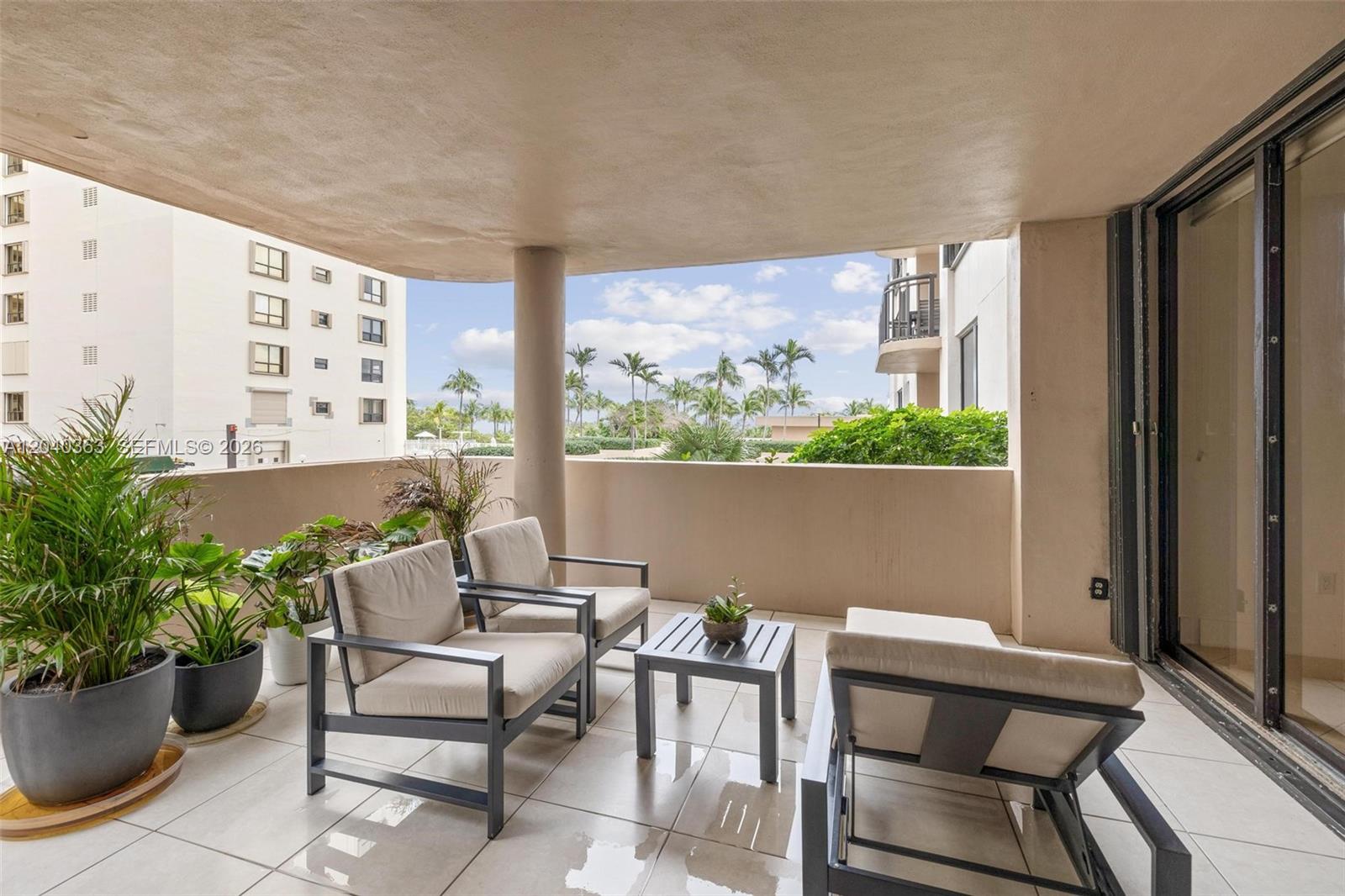 A covered balcony features tiled flooring, two armchairs, a small table, and a lounge chair — 10175 Collins Ave # 103, Bal Harbour FL 33154, BAL HARBOUR, FL