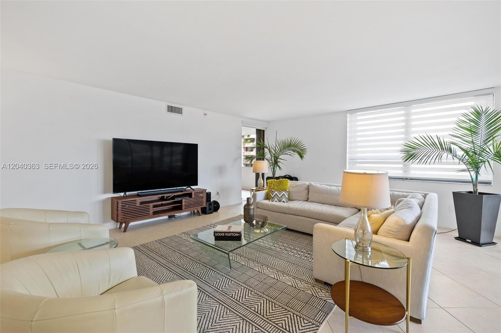A bright living room features a large sectional sofa, glass coffee table, and television console — 10175 Collins Ave # 103, Bal Harbour FL 33154, BAL HARBOUR, FL