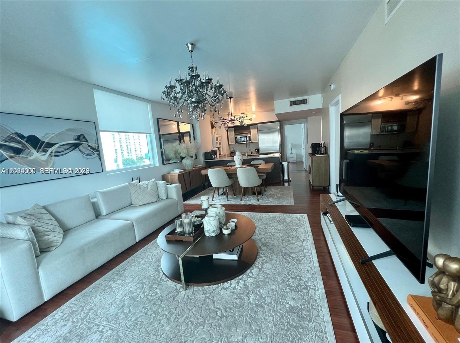A modern living and dining area features a white sofa, round coffee table, and chandelier — 500 Brickell Ave # 1410, Miami FL 33131, MIAMI, FL