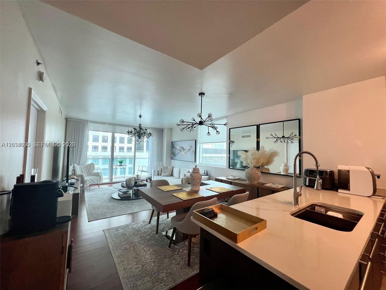 An open-concept living and dining area features a modern kitchen island and contemporary light fixtures — 500 Brickell Ave # 1410, Miami FL 33131, MIAMI, FL