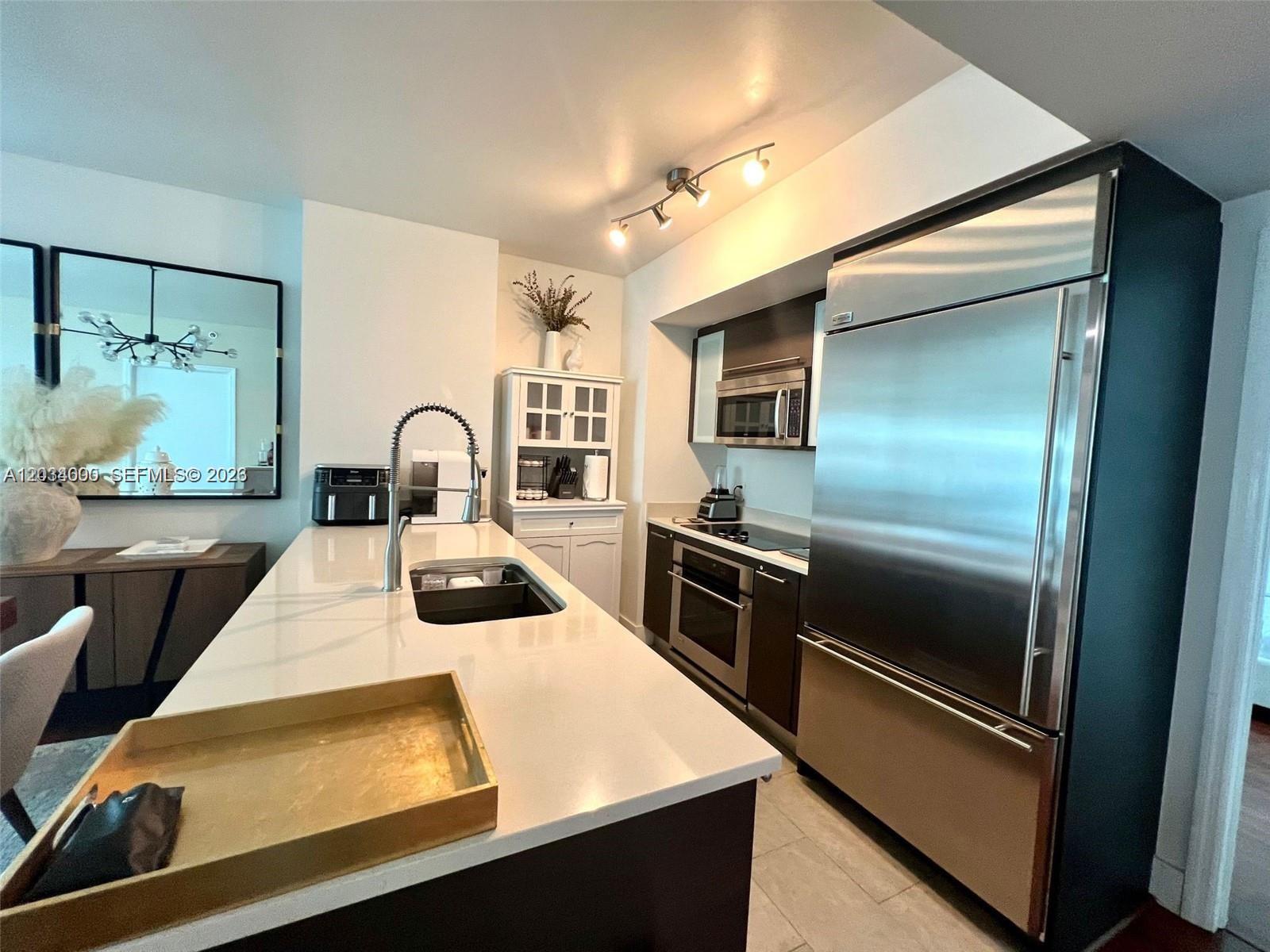 A modern kitchen features a large island with a sink, stainless appliances, and dark cabinetry — 500 Brickell Ave # 1410, Miami FL 33131, MIAMI, FL