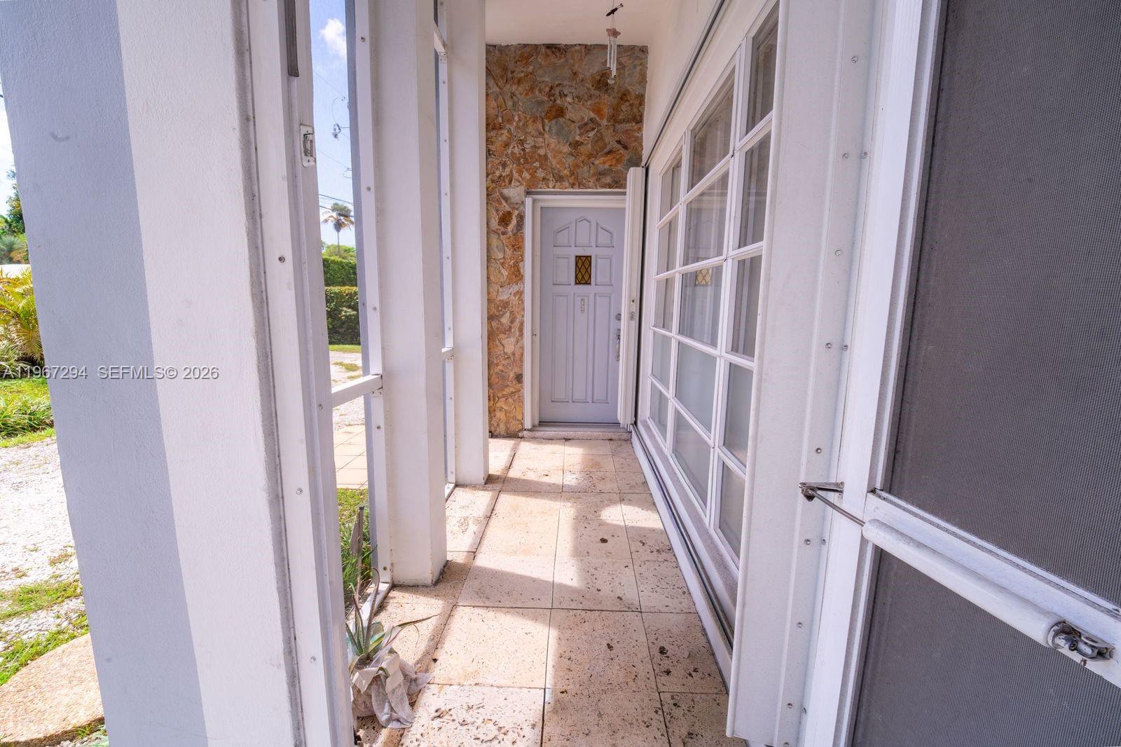 A covered outdoor walkway features a light-colored door, stone wall, and tiled flooring — 11600 NE 6th Ave, Biscayne Park FL 33161, BISCAYNE PARK, FL