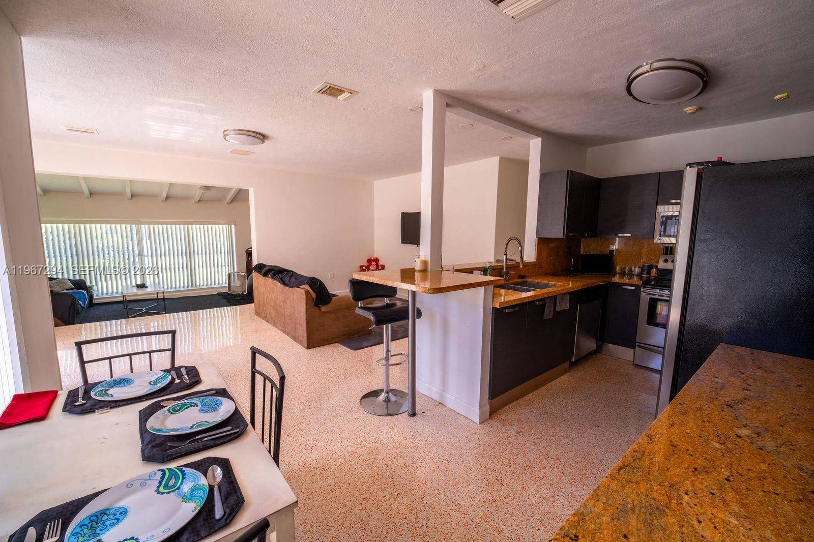A kitchen with granite countertops and a breakfast bar overlooks a dining and living area — 11600 NE 6th Ave, Biscayne Park FL 33161, BISCAYNE PARK, FL