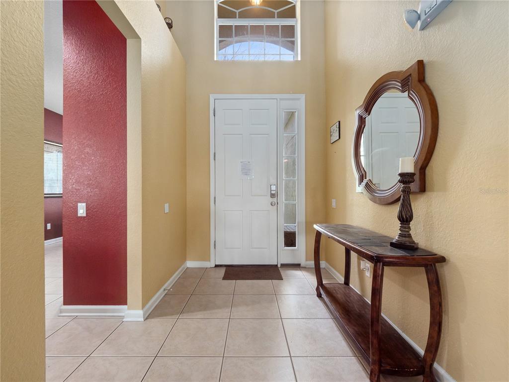 A tiled entryway features a white front door, a wooden console table, and a wall mirror — 2615 PAWNALL STREET, KISSIMMEE, FL