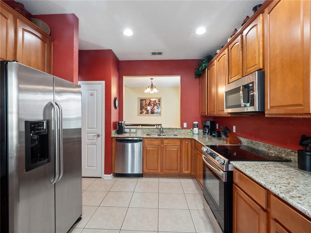 A kitchen features wood cabinets, granite countertops, stainless steel appliances, and red walls — 2615 PAWNALL STREET, KISSIMMEE, FL