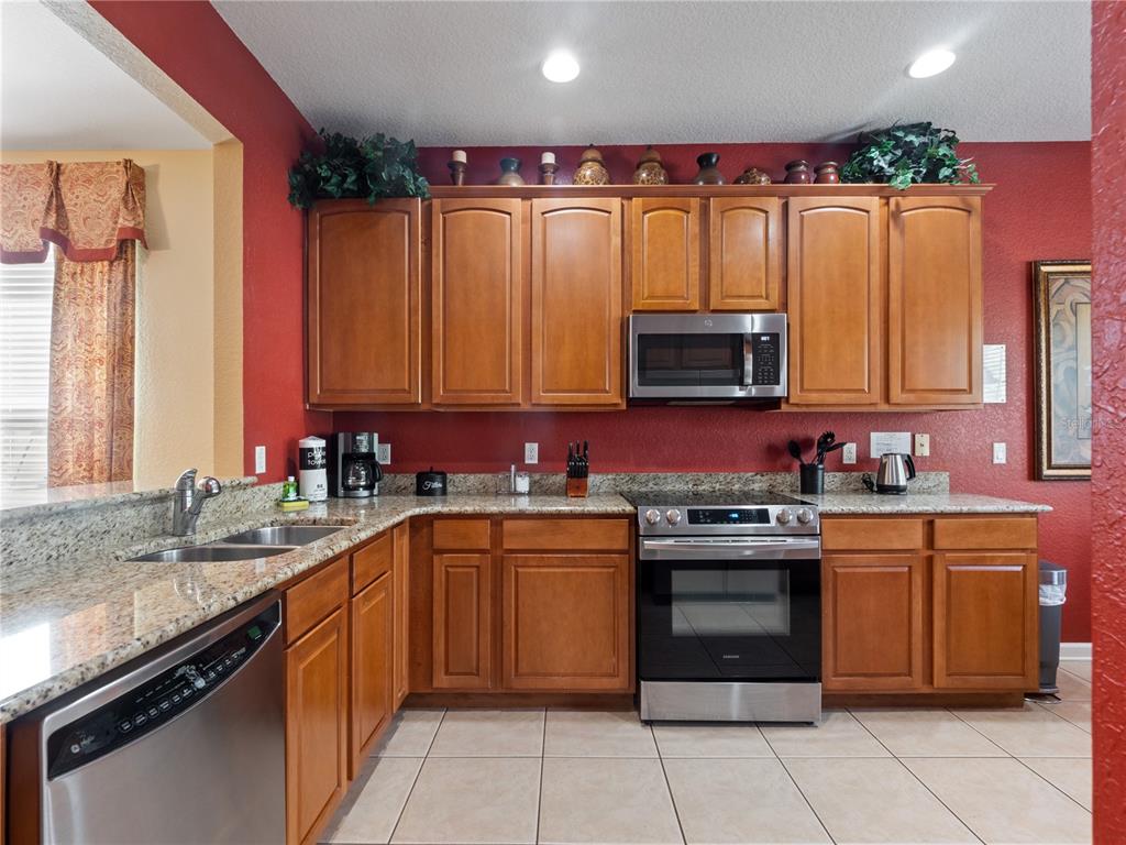 A kitchen features wood cabinets, granite countertops, stainless steel appliances, and red walls — 2615 PAWNALL STREET, KISSIMMEE, FL