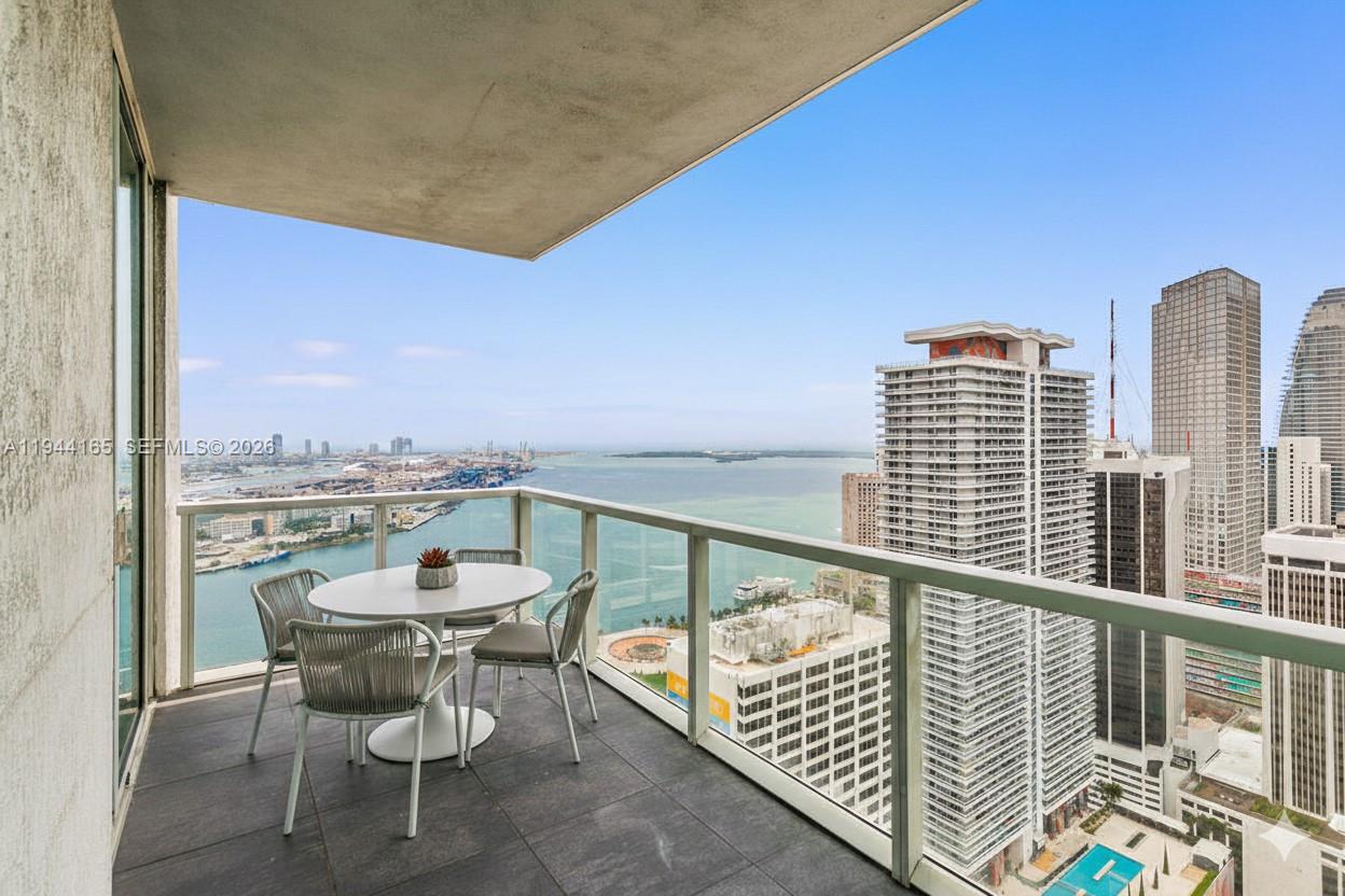 A high-rise balcony features a small dining set overlooking a city skyline and bay — 253 NE 2nd St # 4608, Miami FL 33132, MIAMI, FL