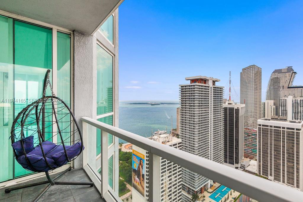 A balcony with a hanging chair overlooks a city skyline and a large body of water — 253 NE 2nd St # 4608, Miami FL 33132, MIAMI, FL