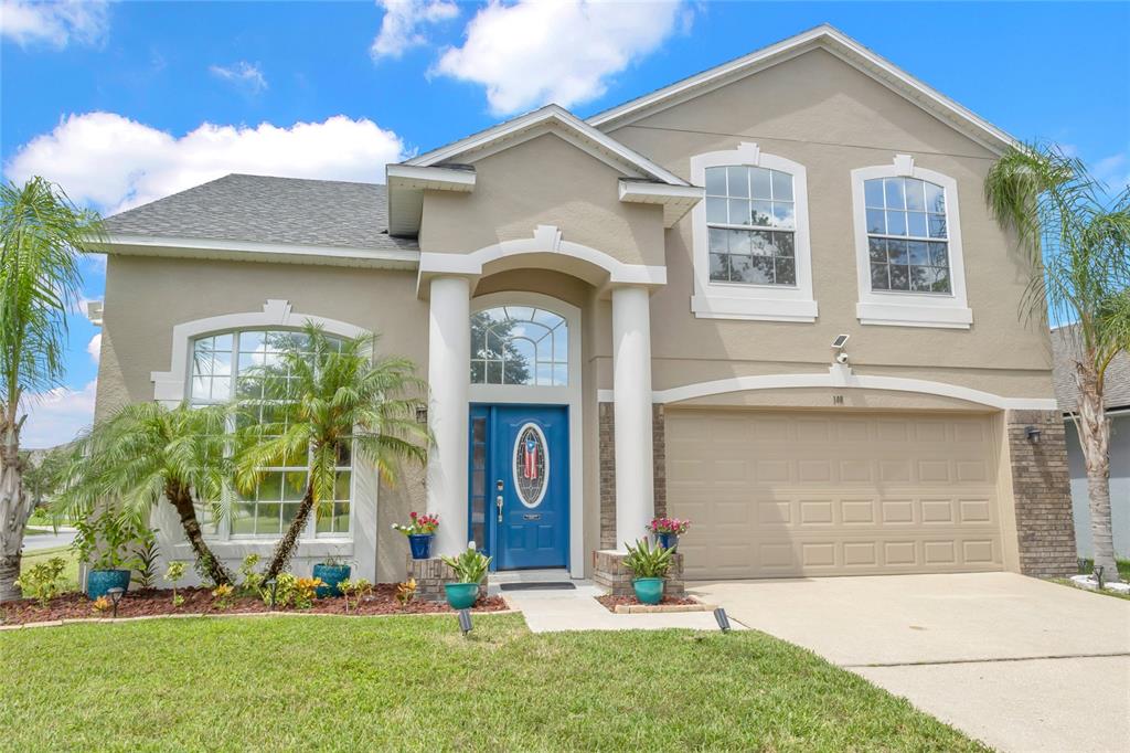 A two-story suburban house with a blue front door, tan stucco exterior, and a garage — 100 THORNBURY LANE, KISSIMMEE, FL
