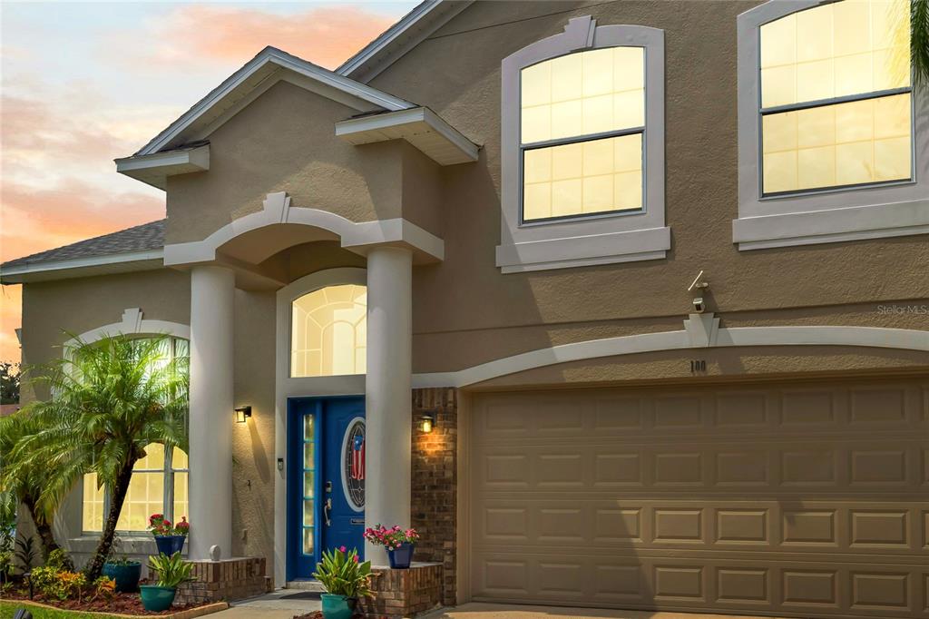 The exterior of a two-story tan house features a blue front door and garage — 100 THORNBURY LANE, KISSIMMEE, FL